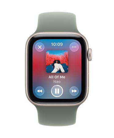 Apple Watch dalam warna Titanium Emas dengan tali jam loop Milan, wajah jam menampilkan Apple Music yang sedang diputar, kontrol Liquid Glass tembus pandang