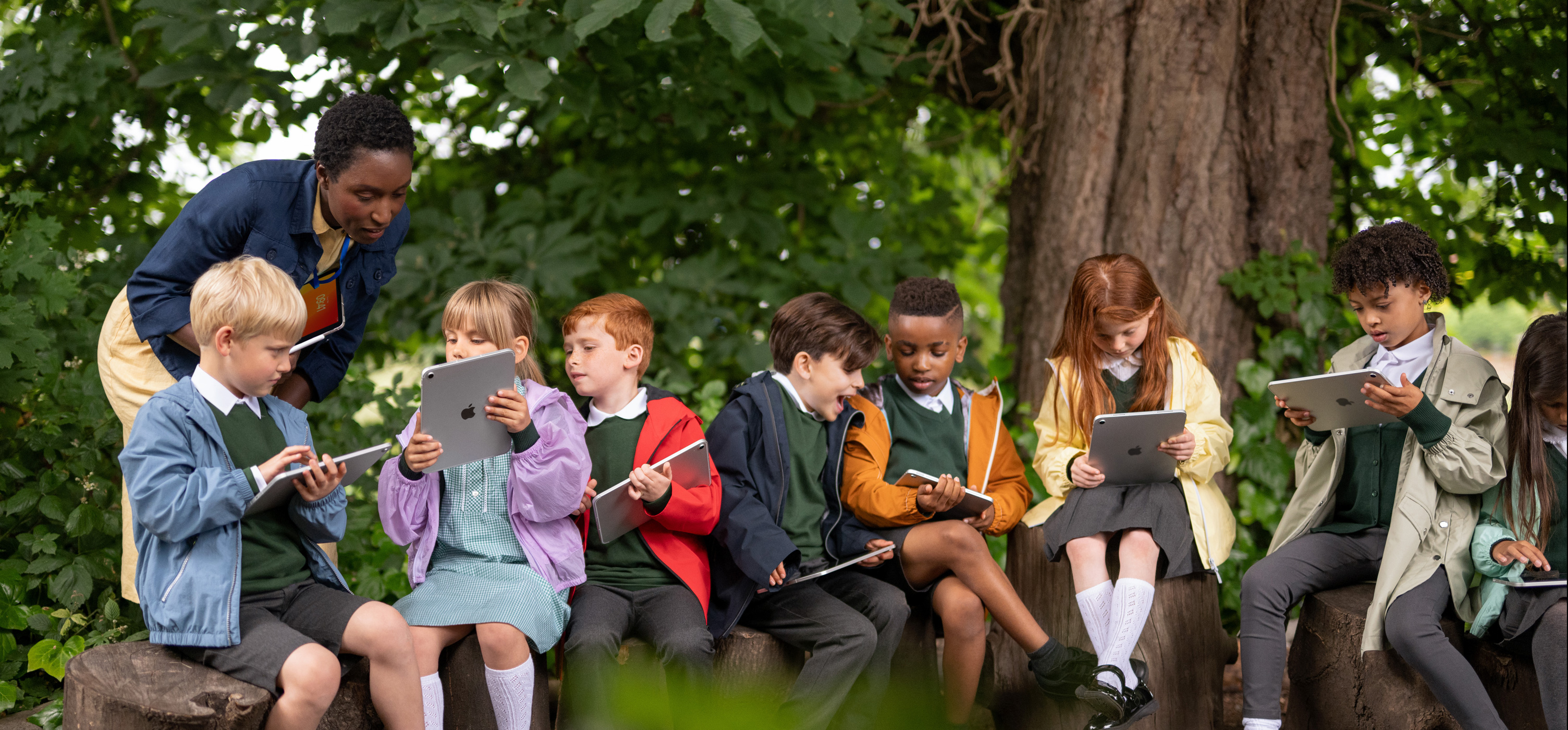 A group of young students use iPad outdoors as an educator guides them while holding an iPad, highlighting mobility to learn anywhere