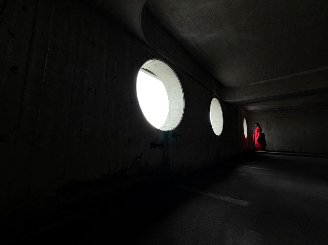 Een vrouw in een lange rode jurk wordt in een lege ruimte gefotografeerd. De Camera-app wisselt van brandpuntsafstanden om de mogelijkheden van het pro-camerasysteem te laten zien. Hier gekozen brandpuntsafstand: 13 mm