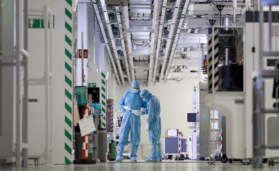 Two employees wearing full-body work suits stand in the hallway of a manufacturing facility